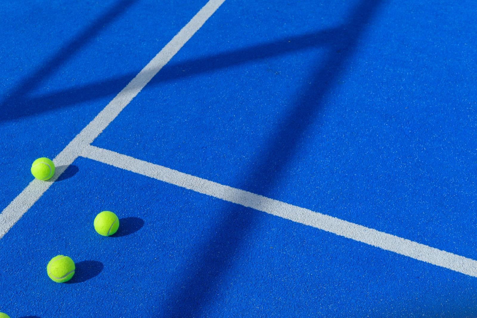 Padel balls resting on the blue court beside the service line