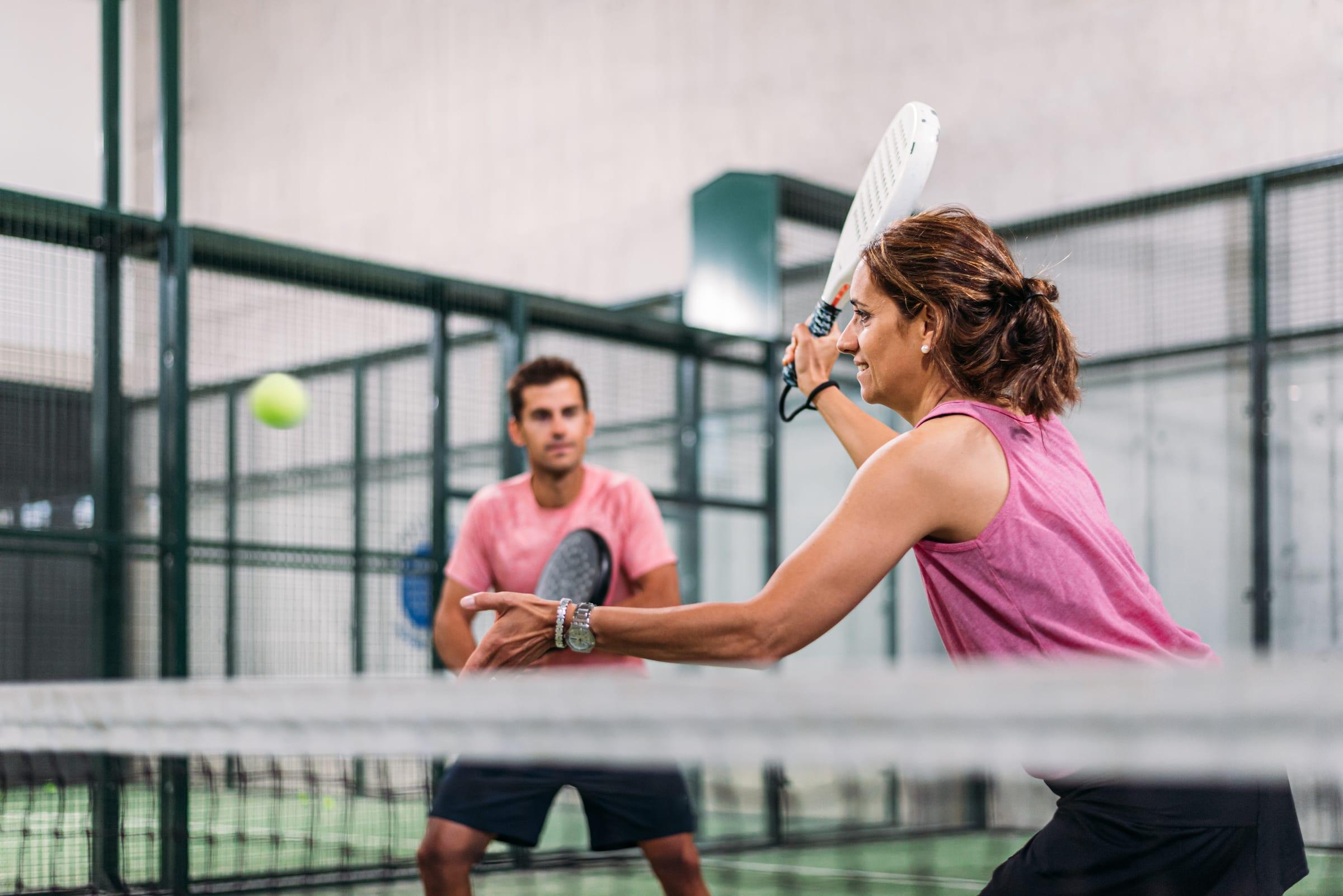 A woman and a man playing a volley at the net on an indoor padel court